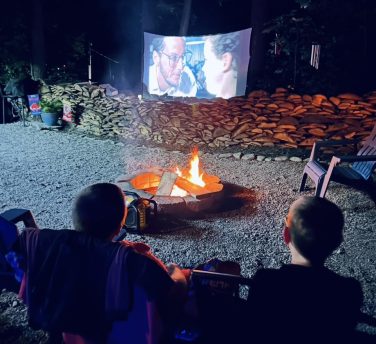 Campers watching a movie by the fire at Sugar Creek Glen Camping in New York