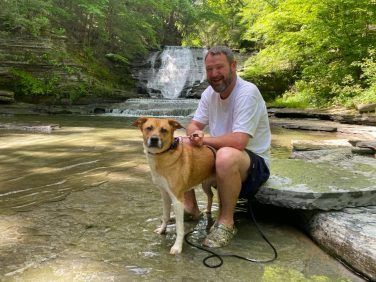 Man sitting with dog at a waterfall near Sugar Creek Glen Camping in New York