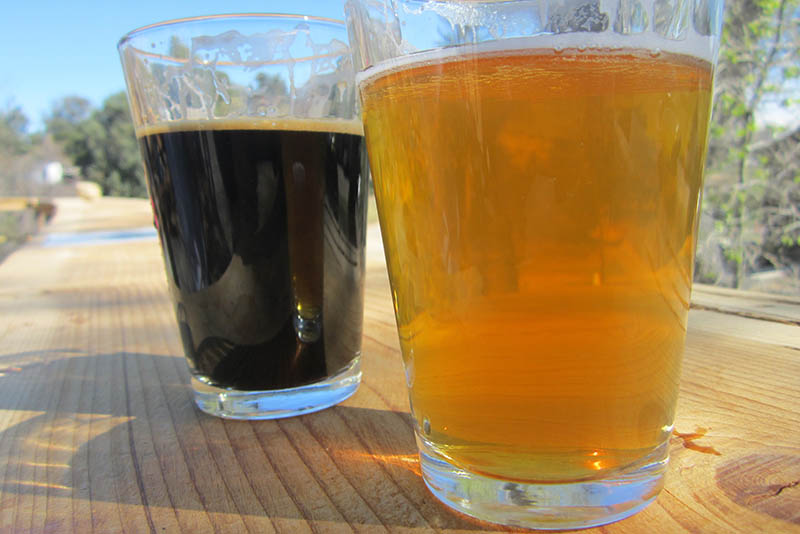 Two glasses of craft beer, one golden and one dark, resting on an outdoor wooden table.