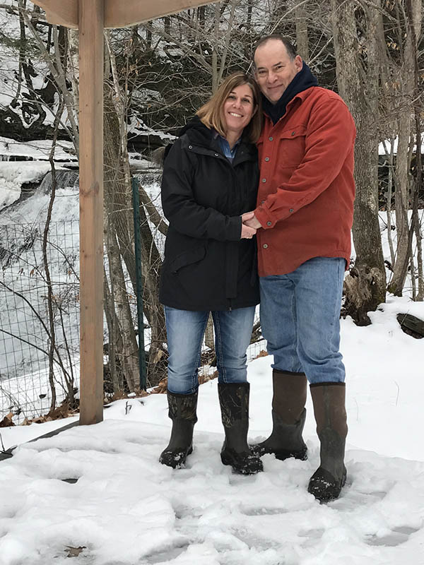 Daniel and Merav, owners of Sugar Creek Glen Campground, standing together near a snow-covered waterfall in Dansville, NY.