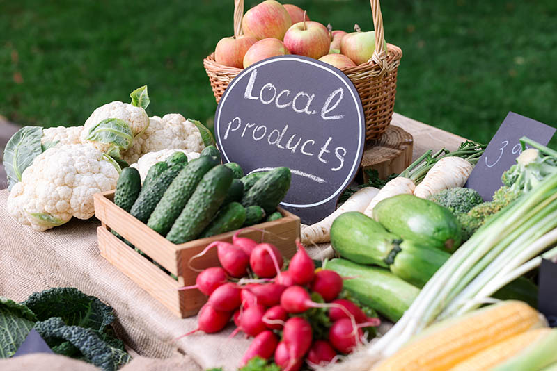 Fresh vegetables, apples, and locally grown produce displayed at a colorful farmers market.