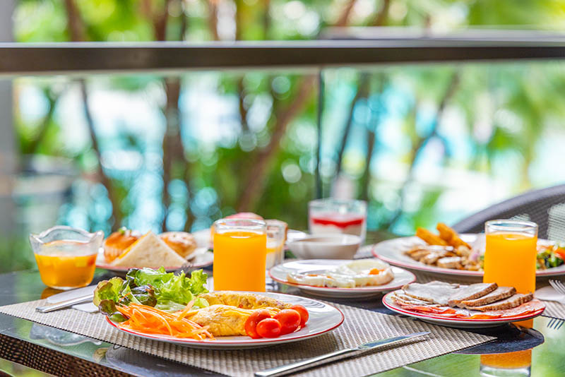 Breakfast dishes, fresh vegetables, and orange juice served on an outdoor restaurant patio.