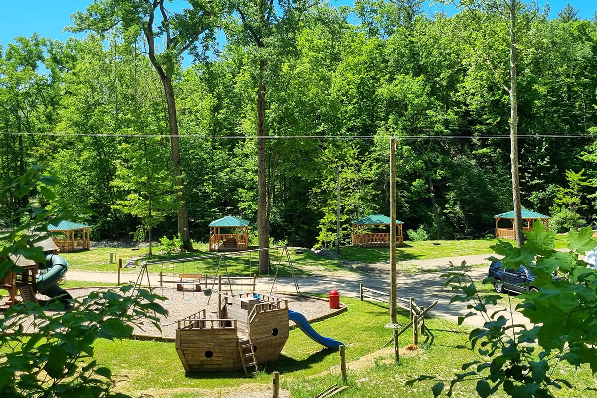 Playground at Sugar Creek Glen Campground featuring a wooden pirate ship, slides, swings, and shaded picnic pavilions.
