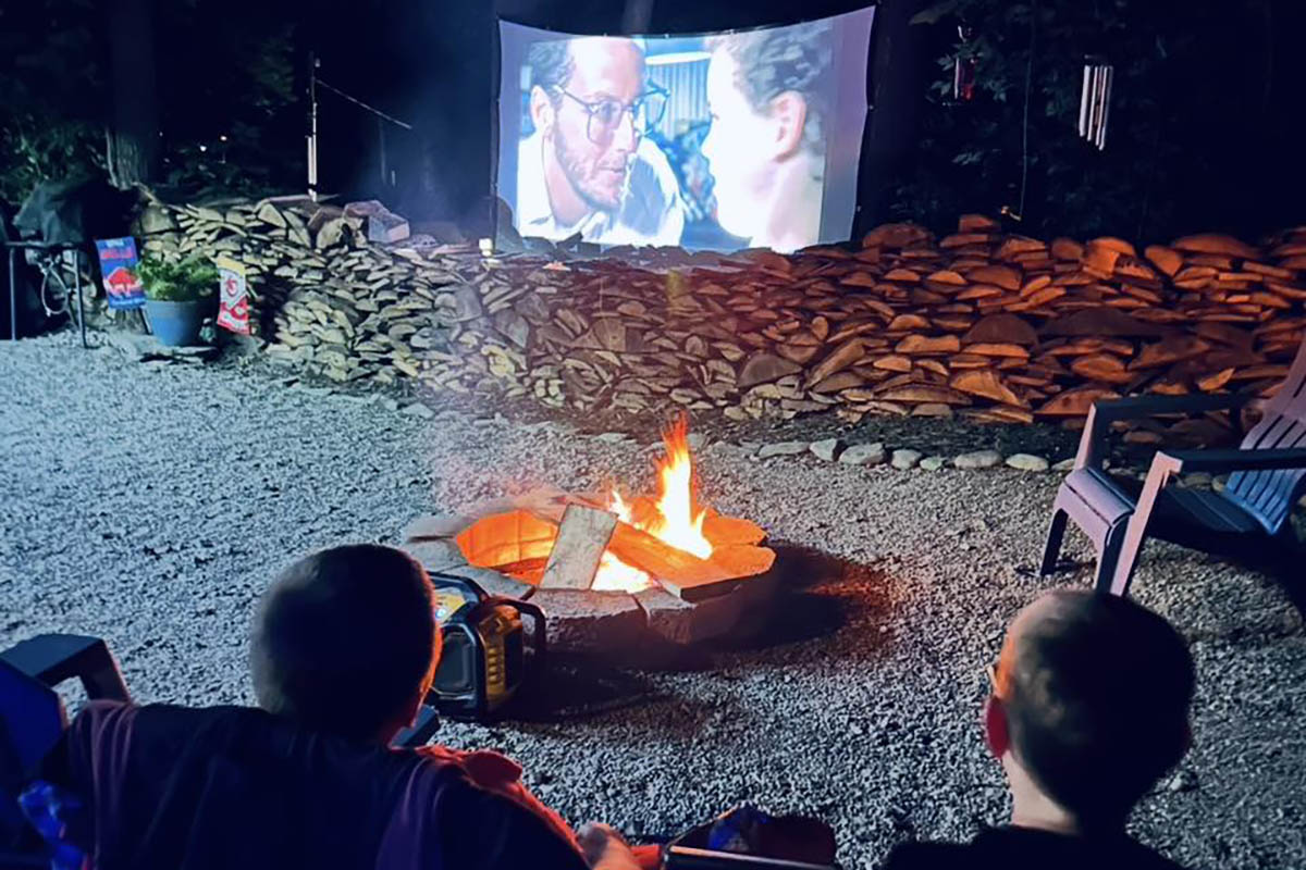 Campers enjoying an outdoor movie beside a campfire at Sugar Creek Glen Campground near Dansville, NY.